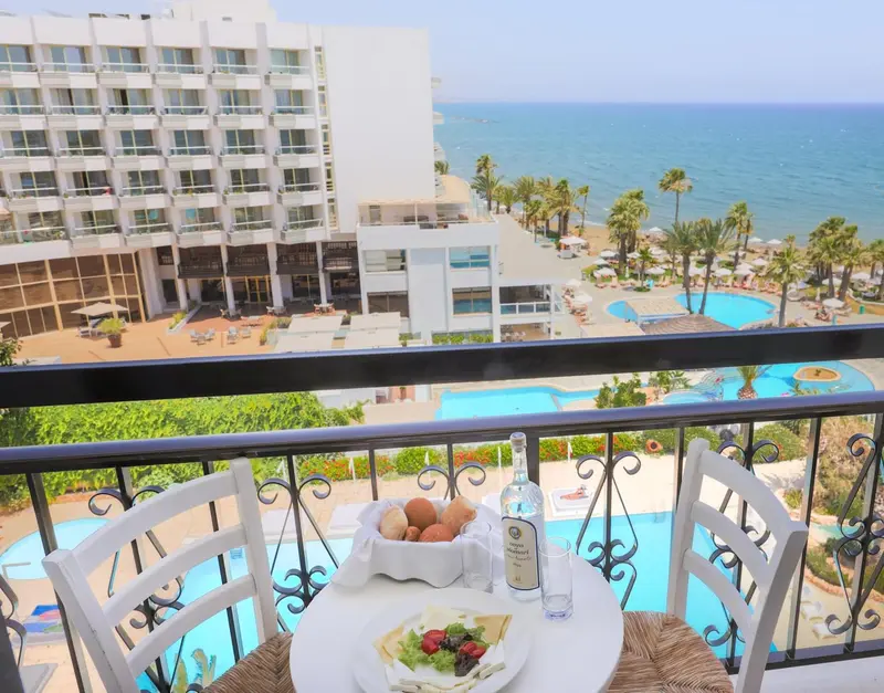 Une table est dressée sur un balcon avec vue sur la mer et une piscine.
