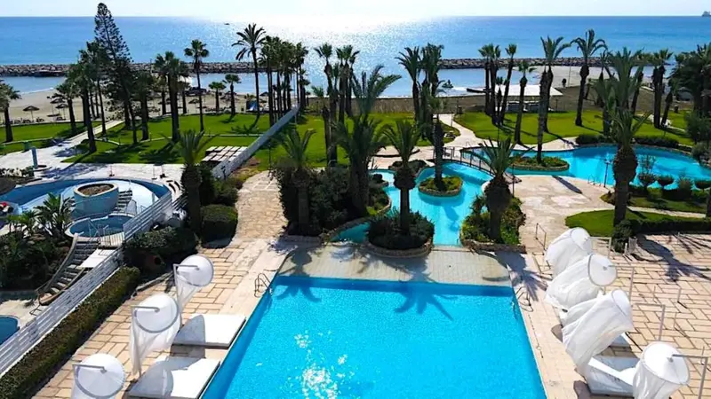Vue aérienne d'un complexe hôtelier avec piscines et végétation luxuriante face à la mer.