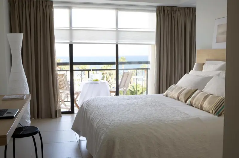 Chambre lumineuse avec un grand lit et une vue sur la mer depuis un balcon.