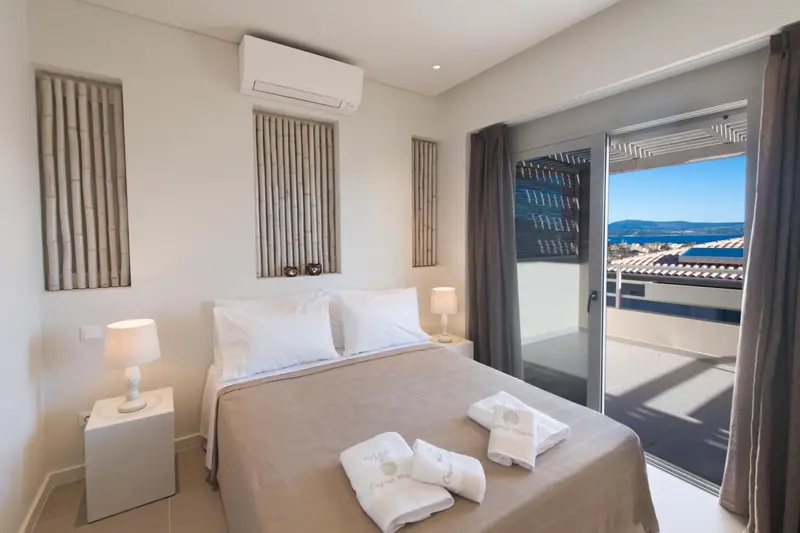 Une chambre lumineuse avec un lit fait et une vue sur la mer par une baie vitrée.