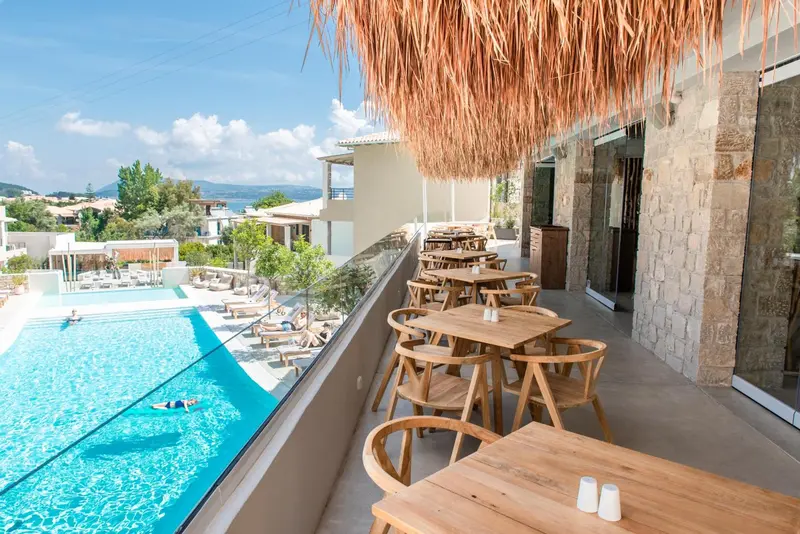 Terrasse ombragée avec tables et chaises donnant sur une piscine et un paysage montagneux.