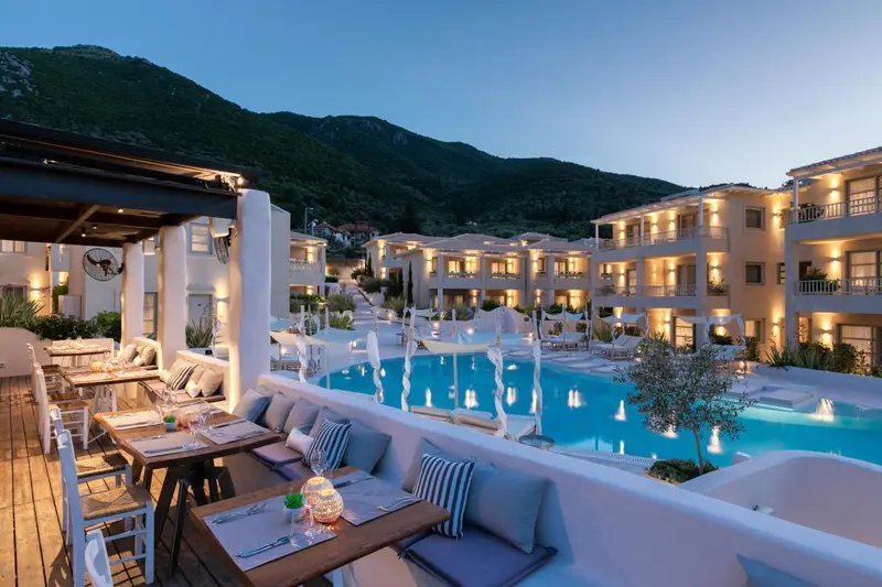 Terrasse de restaurant avec tables dressées devant une piscine et des bâtiments en arrière-plan.