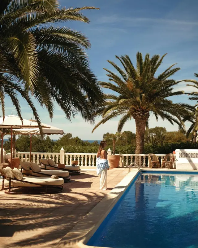 Transats alignés au bord d'une piscine ensoleillée, avec des palmiers en arrière-plan.
