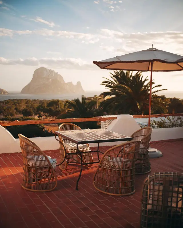 Terrasse avec mobilier en rotin et vue sur la mer et une île rocheuse.