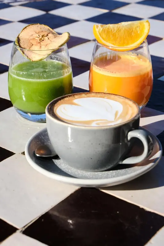Deux jus de fruits et un café au lait sont présentés sur une table à carreaux.