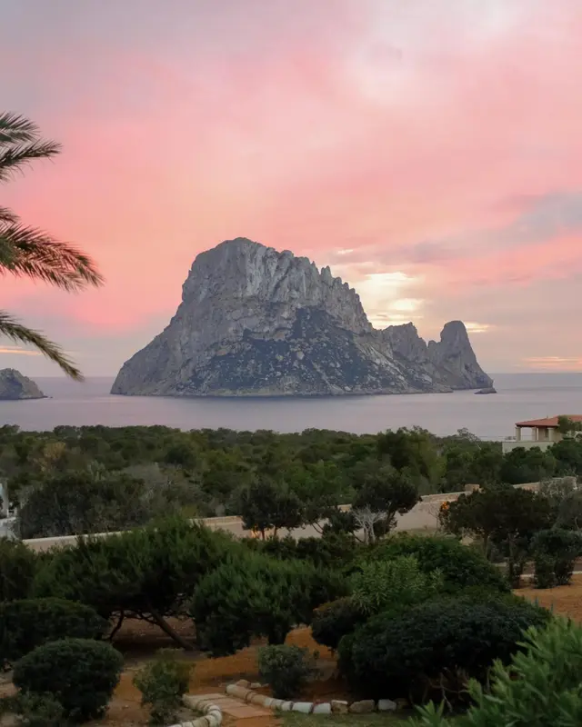 Un paysage côtier avec une formation rocheuse imposante au loin, illuminée par les couleurs du coucher de soleil.
