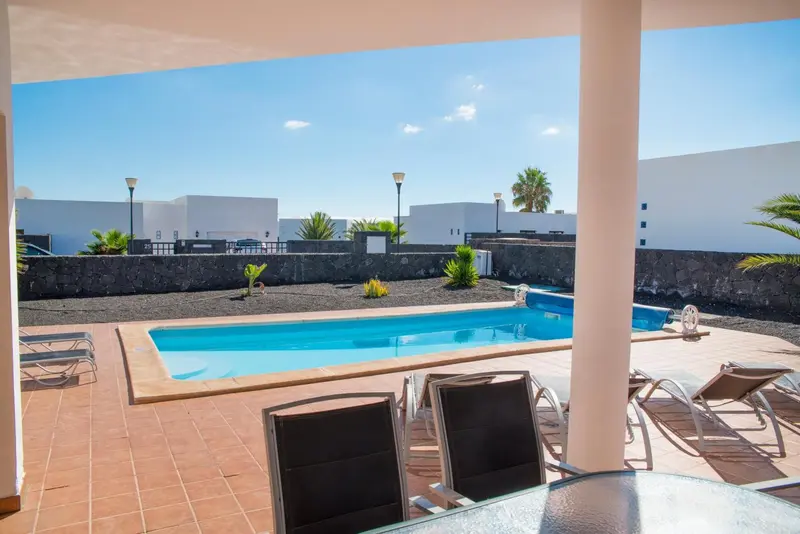 Une piscine rectangulaire avec des transats et des plantes tropicales.