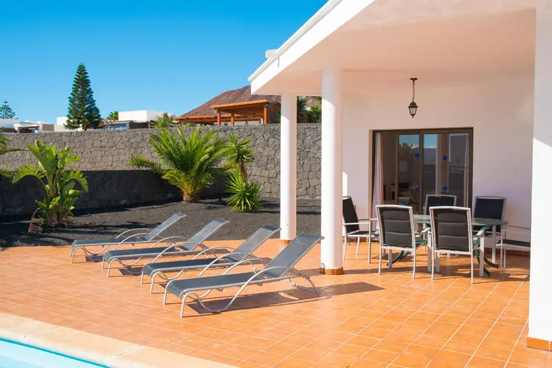 Transats alignés sur une terrasse carrelée devant une maison blanche.