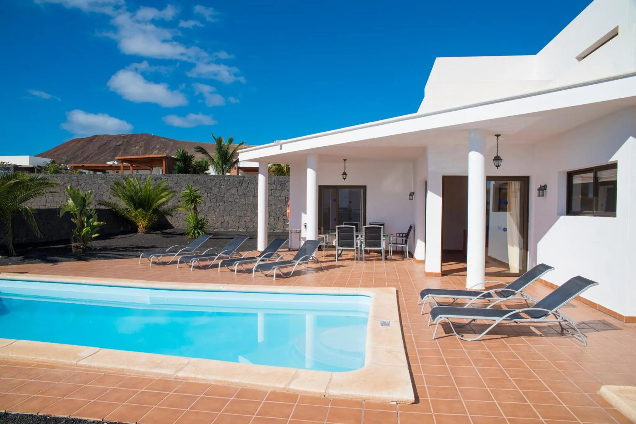 Transats et piscine devant une maison blanche avec une terrasse ombragée.