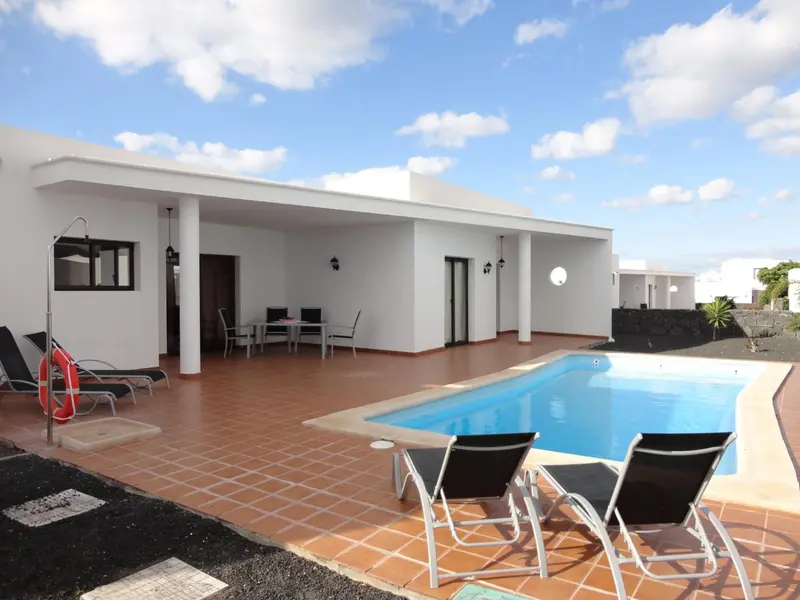 Maison blanche avec terrasse et piscine ensoleillée.
