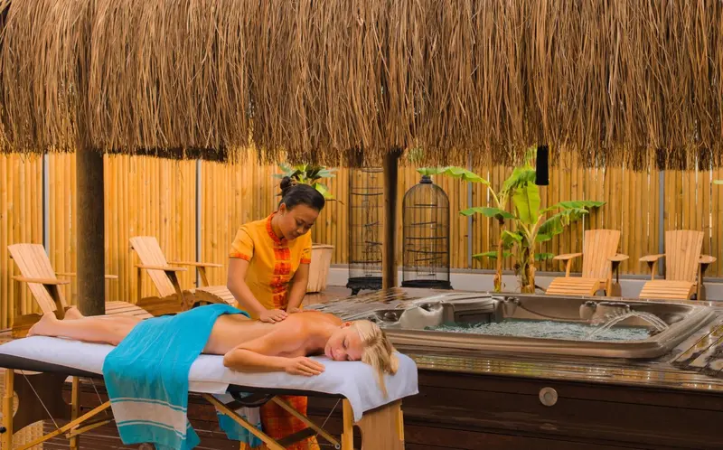 Une femme reçoit un massage en extérieur sur une table, sous une structure en chaume.
