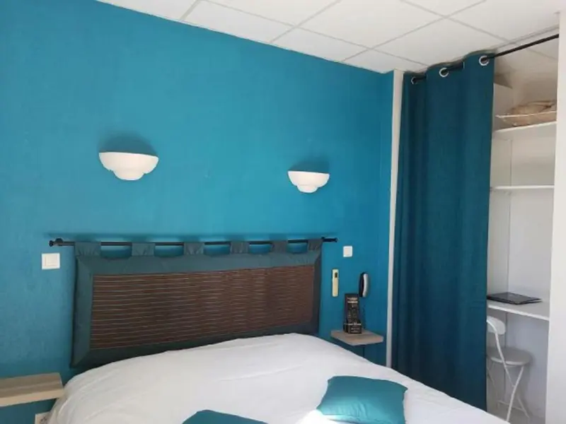 Une chambre avec un lit recouvert d'une courtepointe blanche et de coussins turquoise.