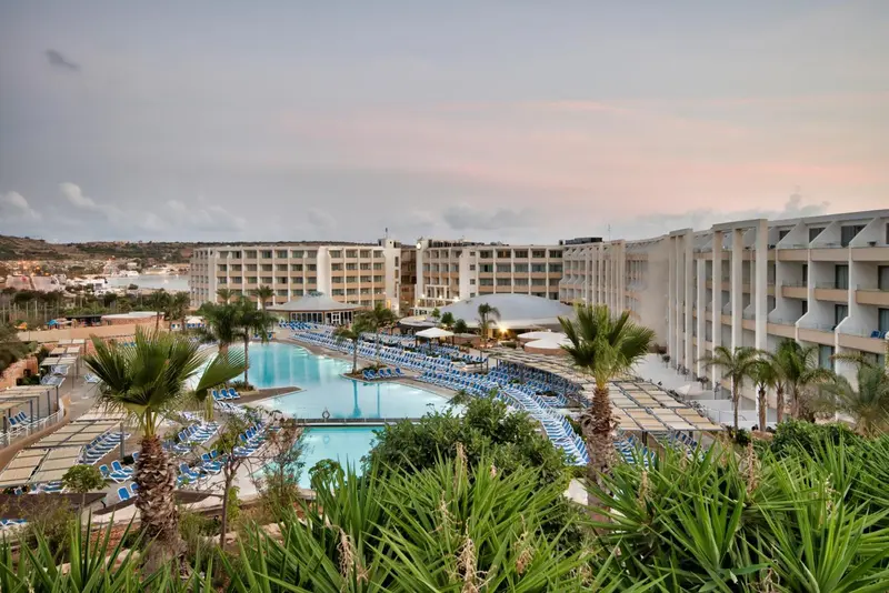 Vue d'un complexe hôtelier avec piscine et végétation luxuriante au coucher du soleil.