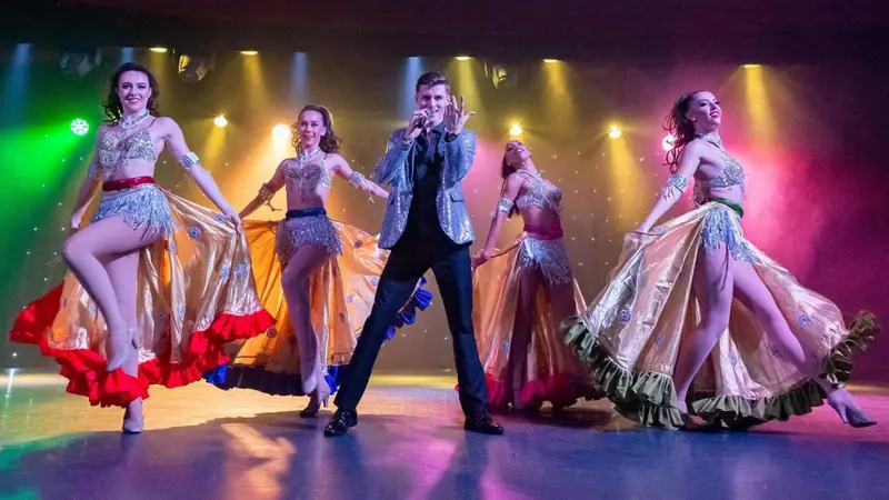Un groupe de danseurs et de chanteurs sur une scène illuminée.