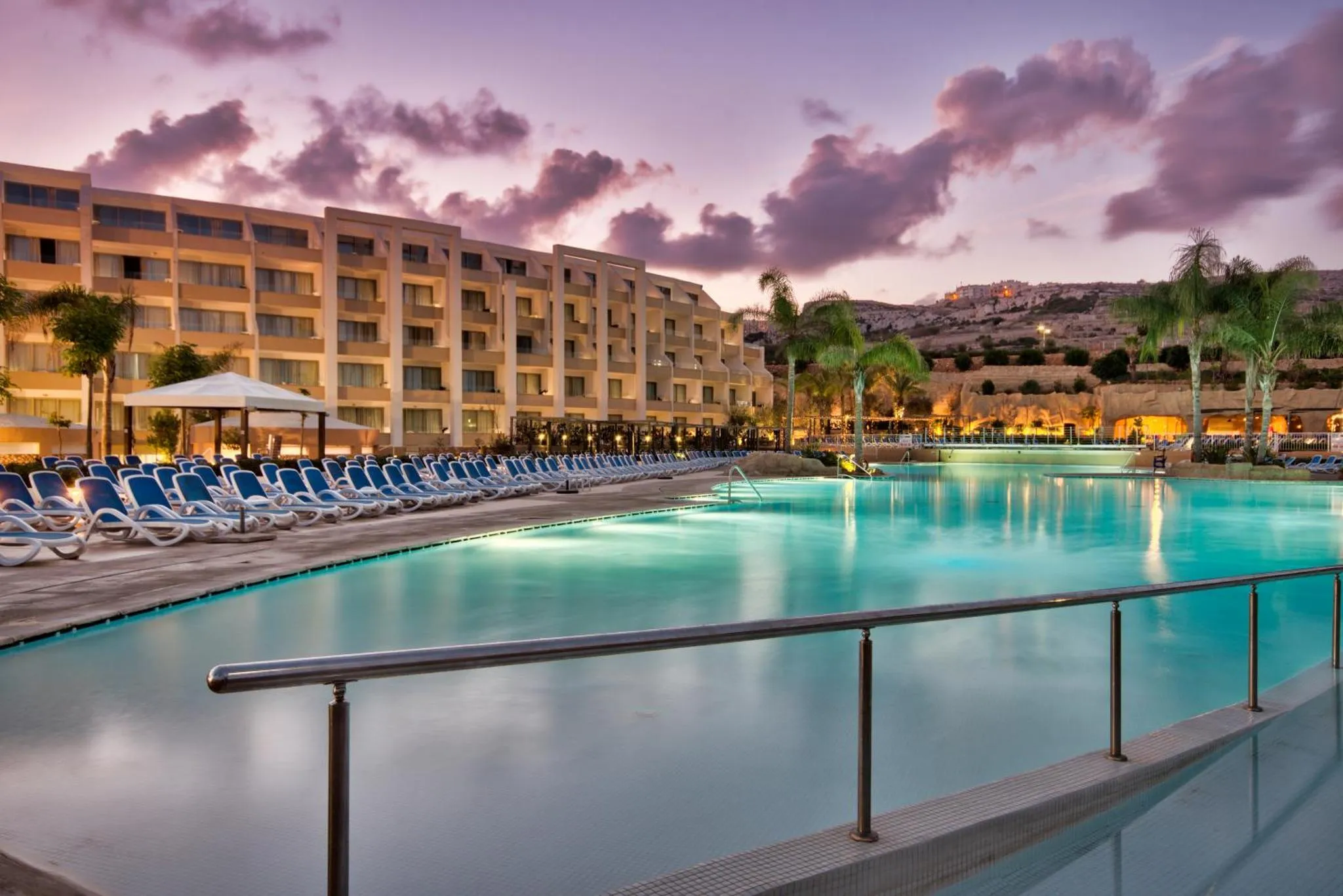 Vue d'une piscine d'hôtel au crépuscule, avec des transats alignés.