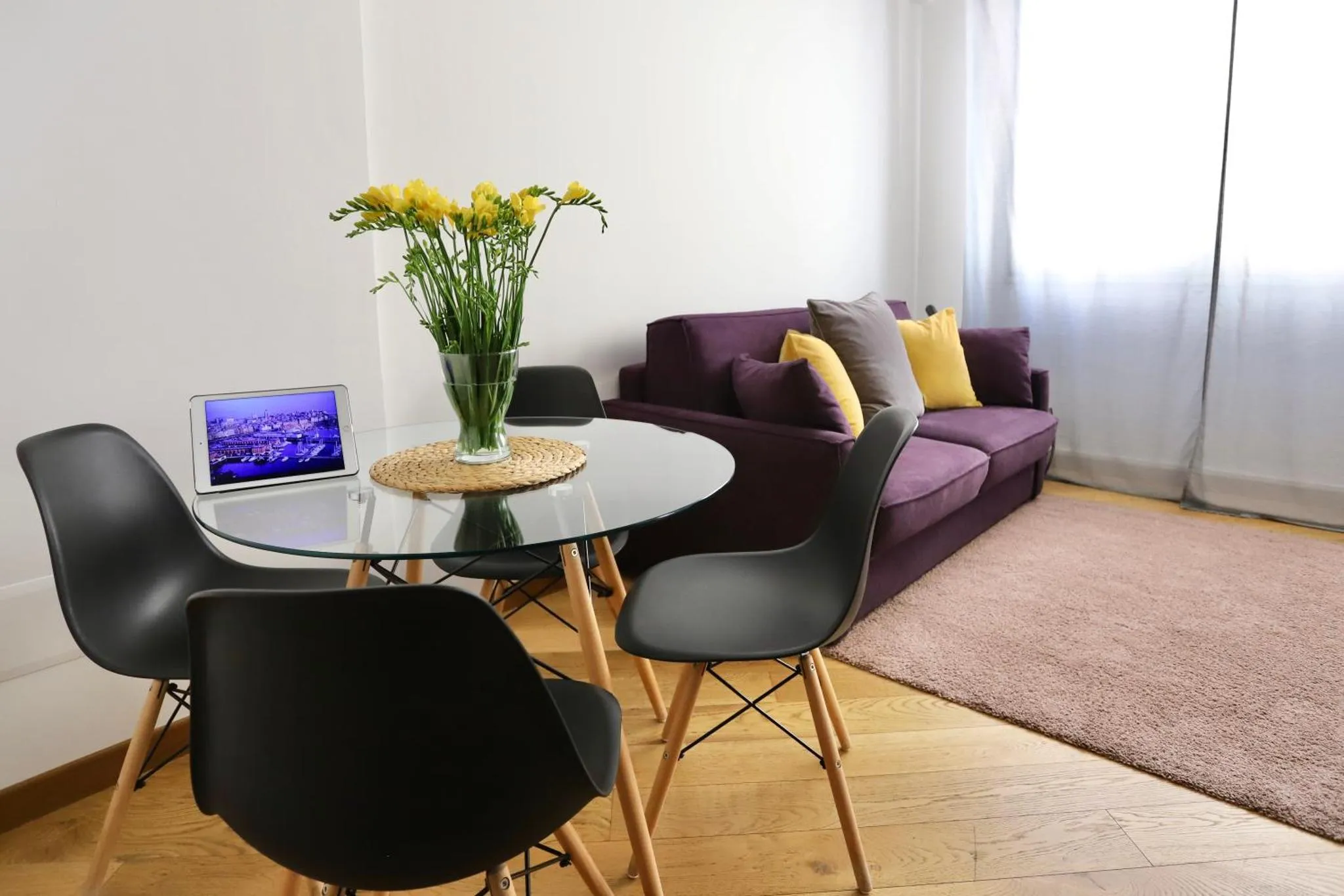 Un salon lumineux avec un canapé violet et une table basse en verre.