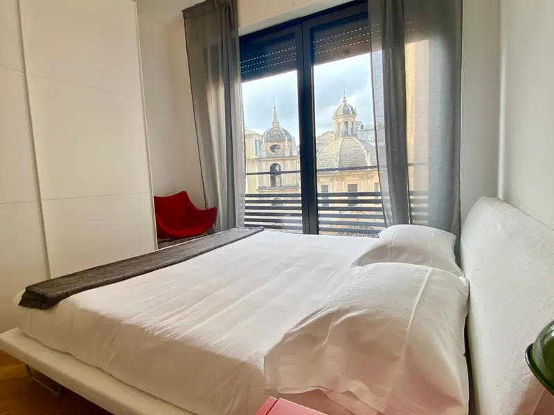 Une chambre lumineuse avec un lit fait et une vue sur un paysage urbain.