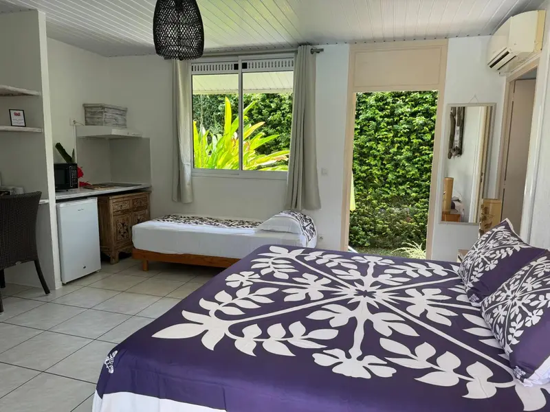 Une chambre lumineuse avec un lit recouvert d'une courtepointe violette et un coin cuisine.