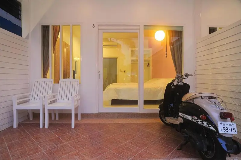 Terrasse carrelée avec mobilier blanc devant une porte vitrée ouverte sur une chambre.