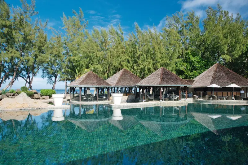 Des parasols de chaume surplombent une piscine turquoise bordée de végétation.