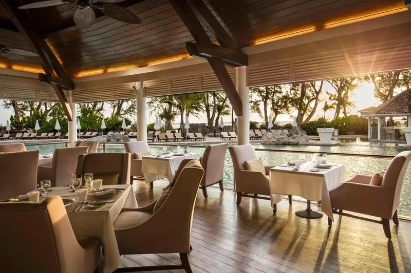 Une salle à manger lumineuse avec des tables dressées face à une piscine et une plage.