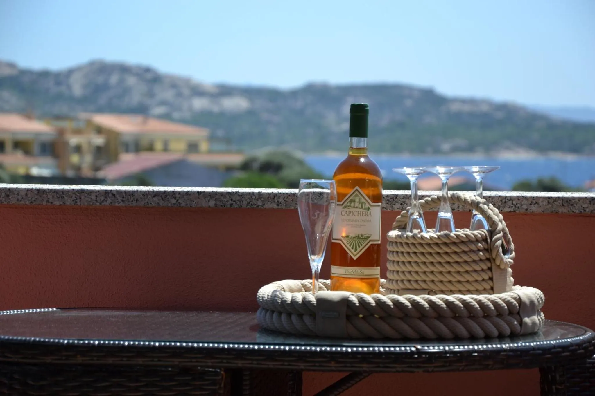 Une bouteille et des verres sur une terrasse avec vue sur la mer et les collines.