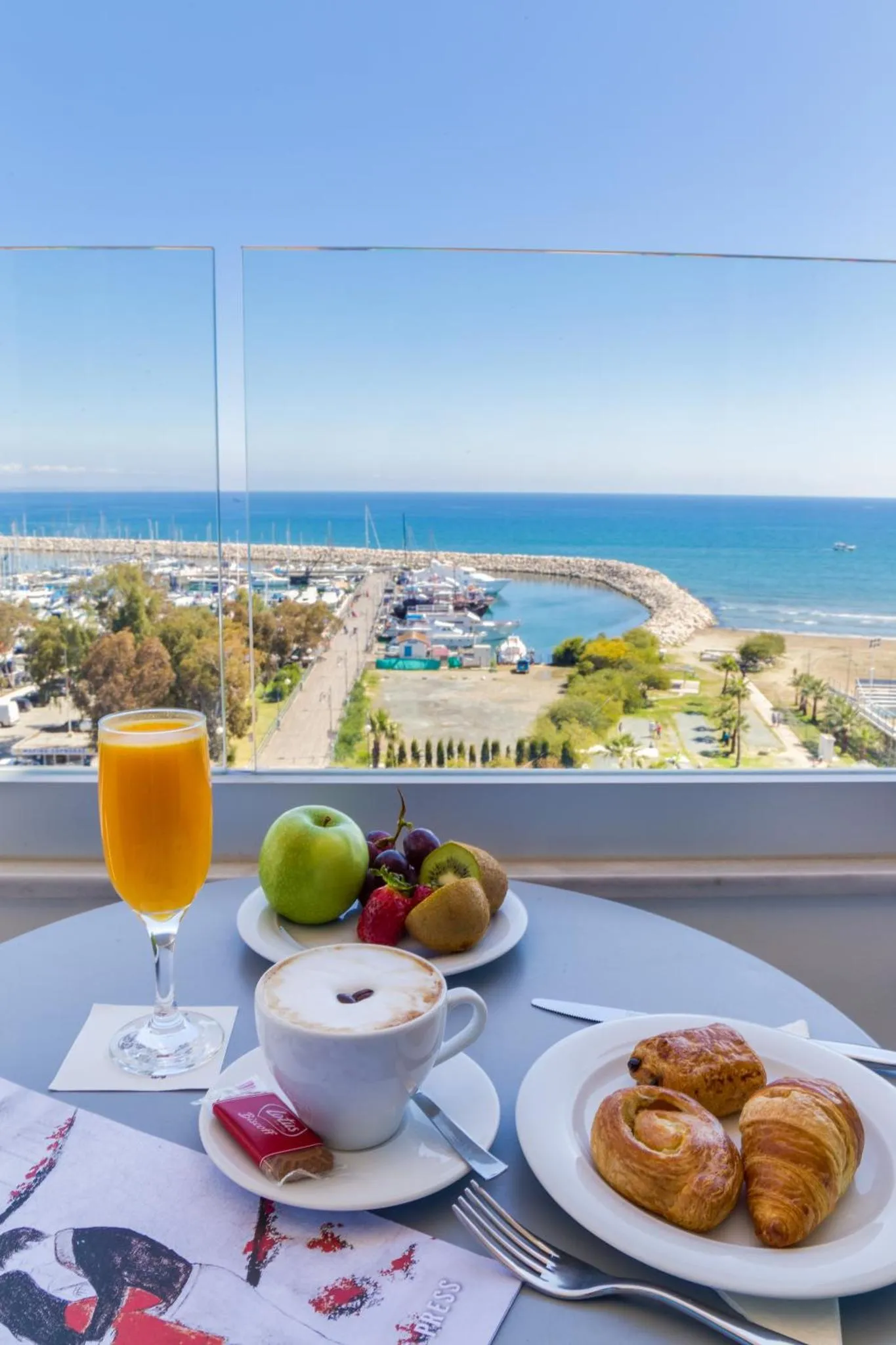 Une table avec un petit-déjeuner est placée devant une fenêtre offrant une vue sur la mer et un port.