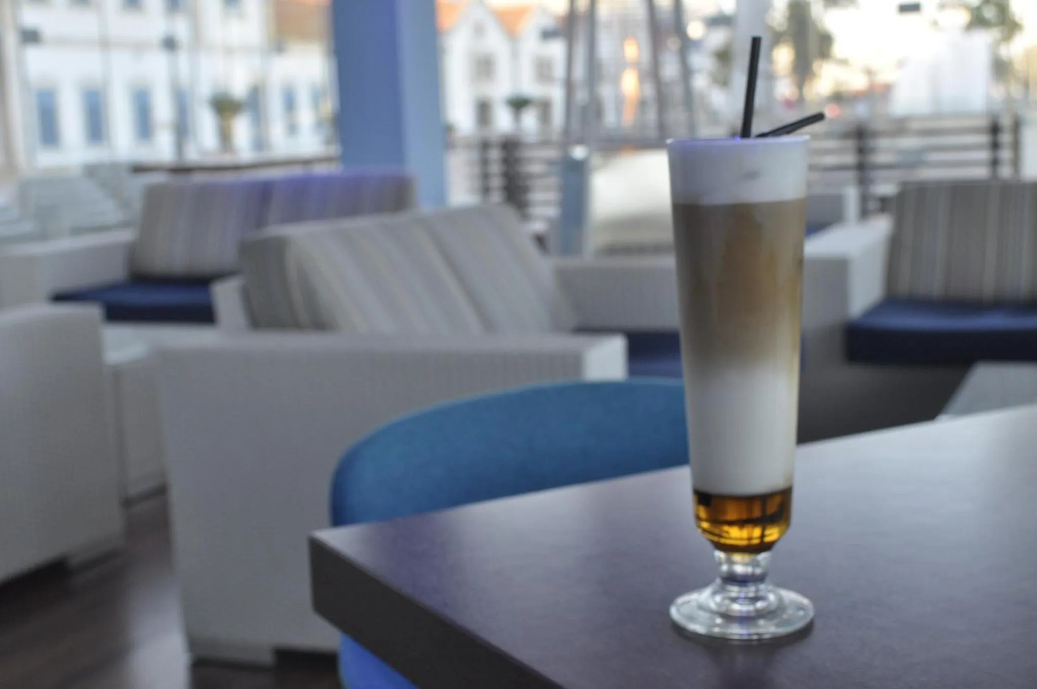 Un verre long et fin rempli d'une boisson en couches est posé sur une table sombre dans un espace lounge.