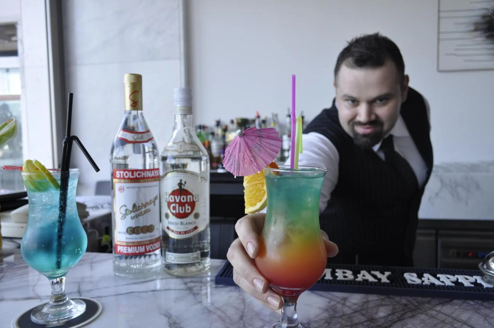 Un barman prépare des cocktails colorés sur un comptoir en marbre.