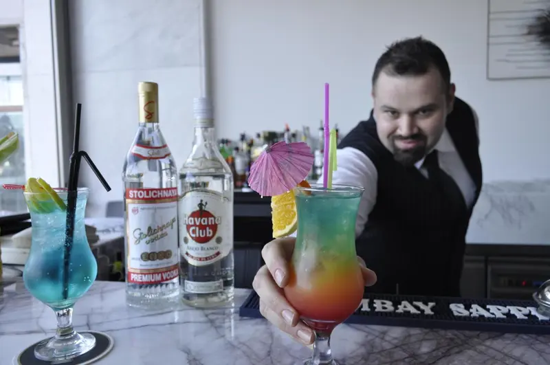 Un barman prépare des cocktails colorés sur un comptoir en marbre.