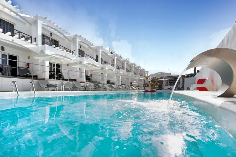 Piscine turquoise avec transats blancs et architecture blanche en arrière-plan.