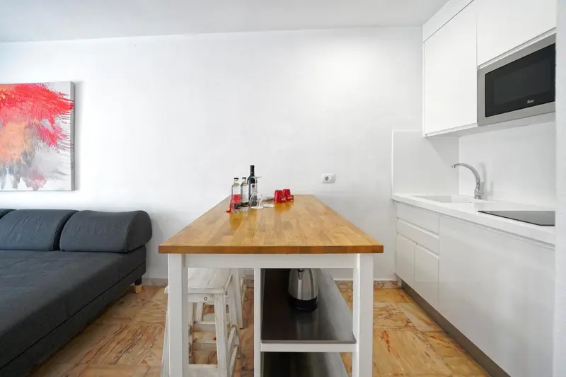 Une table en bois clair dans une pièce lumineuse avec un canapé et une cuisine équipée.