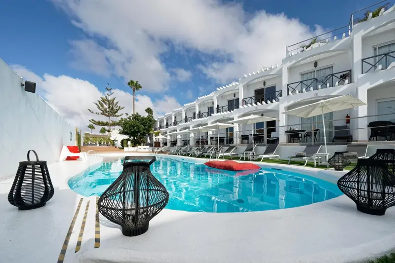 Piscine turquoise bordée de chaises longues et de lanternes décoratives devant un bâtiment blanc.