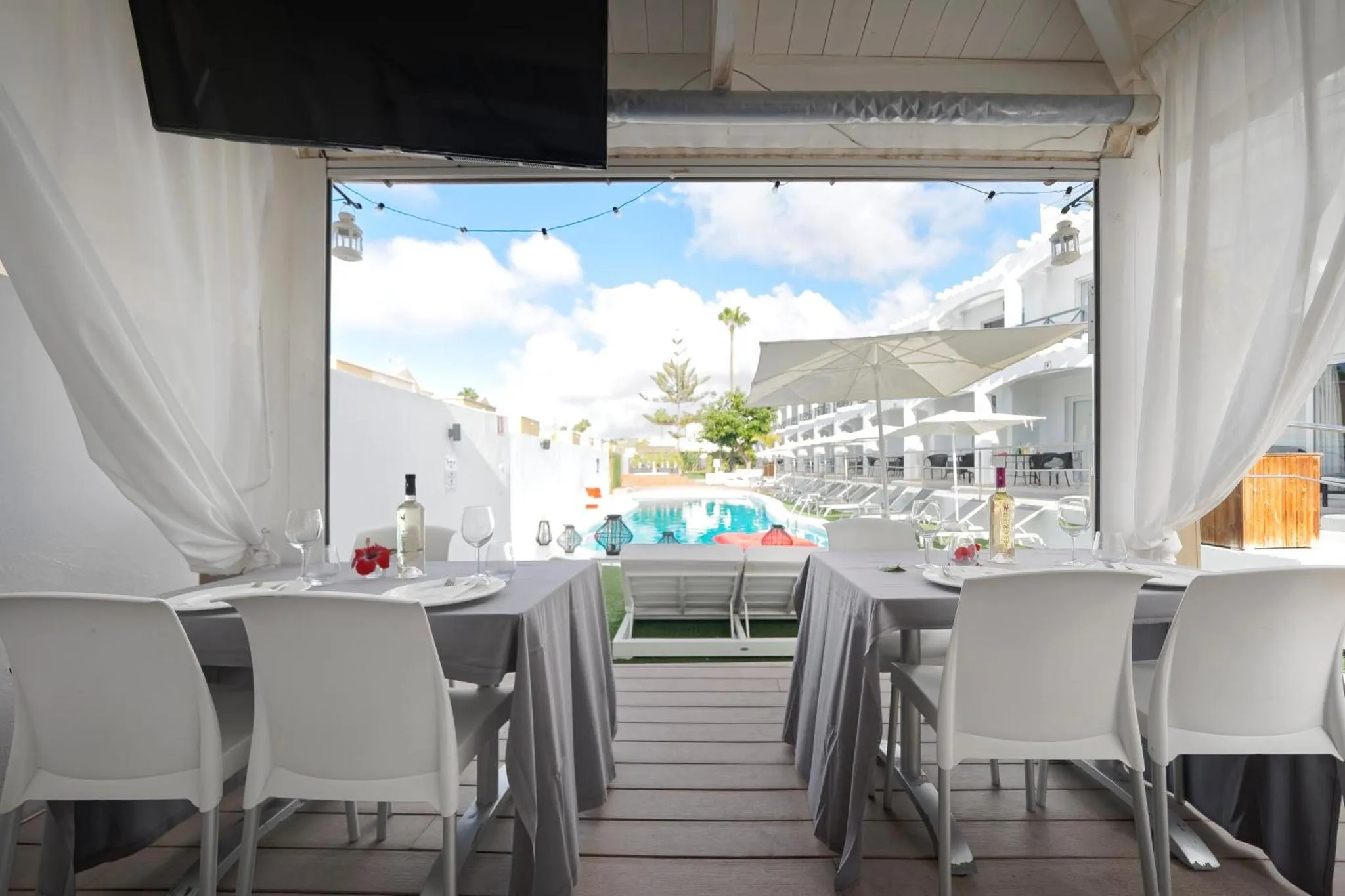 Une table est dressée sur une terrasse ombragée avec vue sur une piscine et des transats.