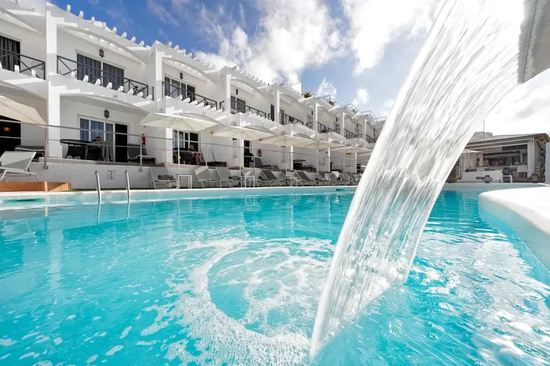 Une cascade d'eau se déverse dans une piscine turquoise bordée de transats blancs.