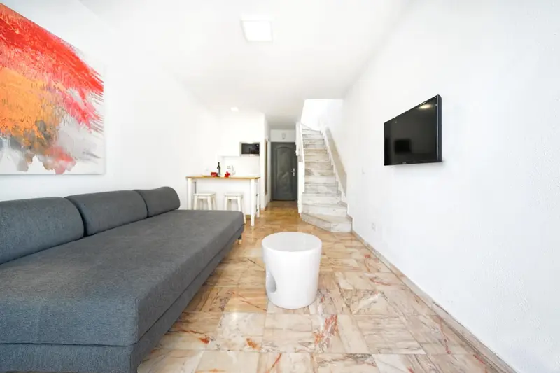 Un canapé gris face à un téléviseur mural dans un intérieur clair.