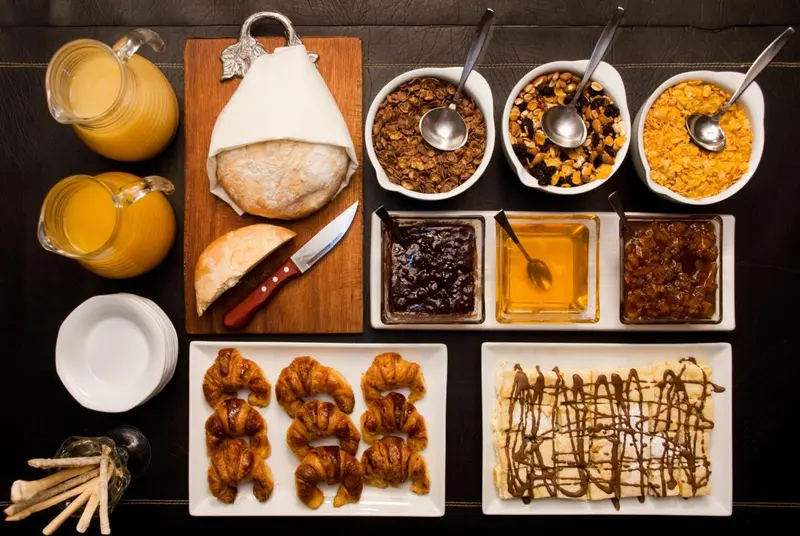 Un plateau de petit-déjeuner avec des viennoiseries, des céréales et des confitures est présenté sur une table sombre.