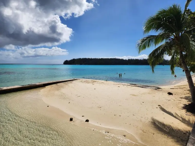 Plage de sable blanc bordée d'eau turquoise sous un ciel nuageux.