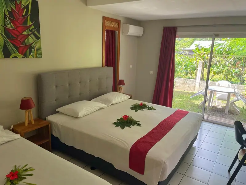 Une chambre avec un grand lit décoré de fleurs et une terrasse accessible par une baie vitrée.