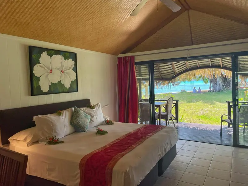 Une chambre avec un grand lit décoré de fleurs, donnant sur une terrasse et la mer.