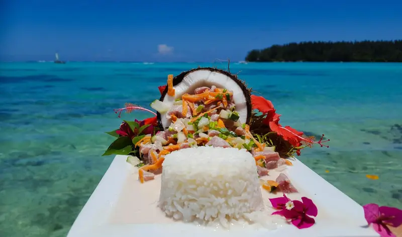 Assiette de riz et de salade de fruits de mer décorée de fleurs sur une plage tropicale.