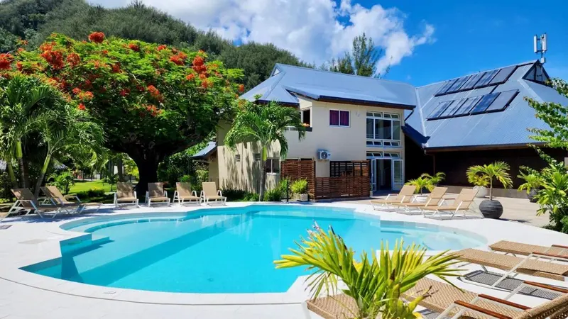 Une piscine turquoise est entourée de chaises longues dans un jardin tropical.