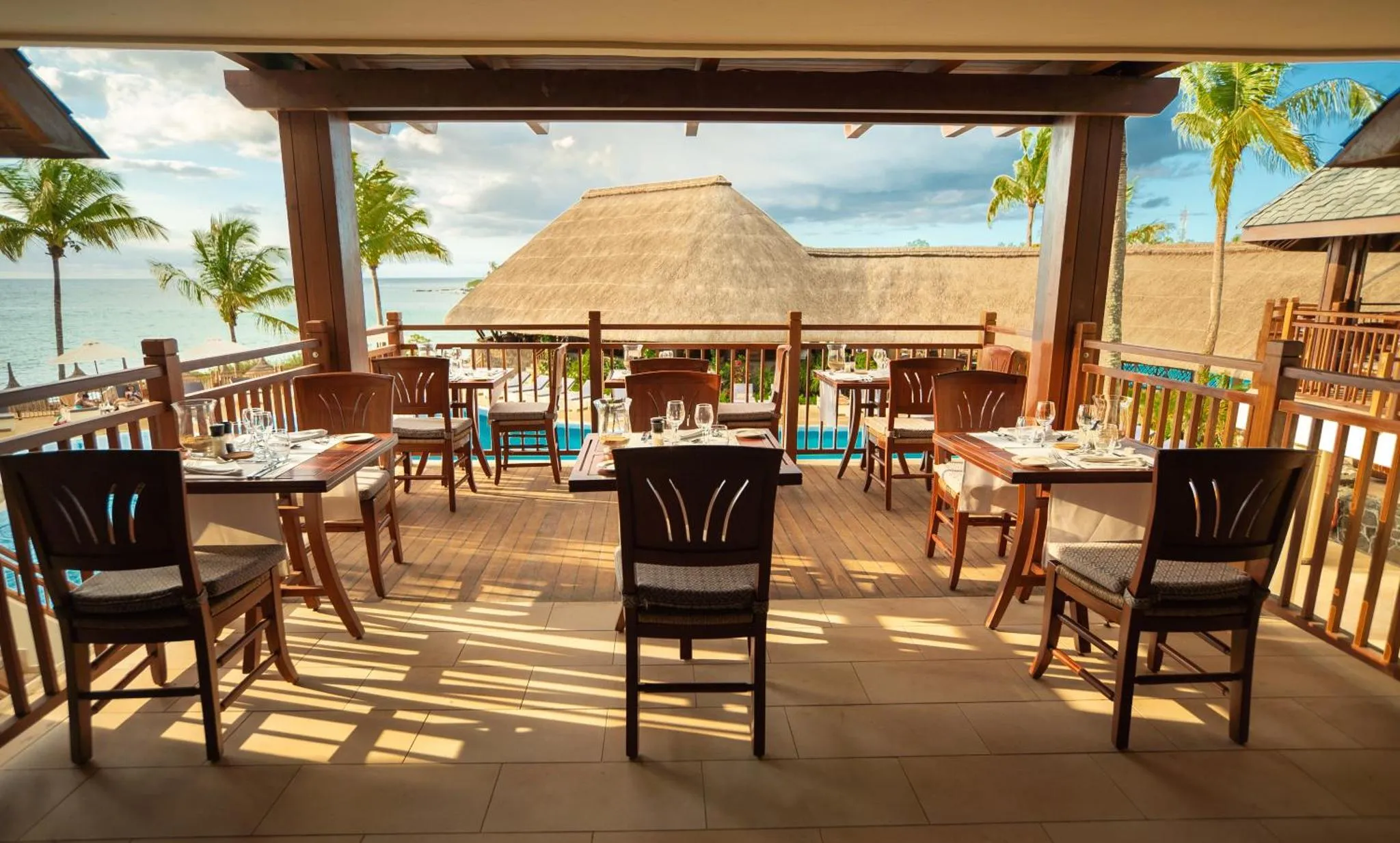 Une terrasse ombragée abrite des tables de restaurant face à la mer.