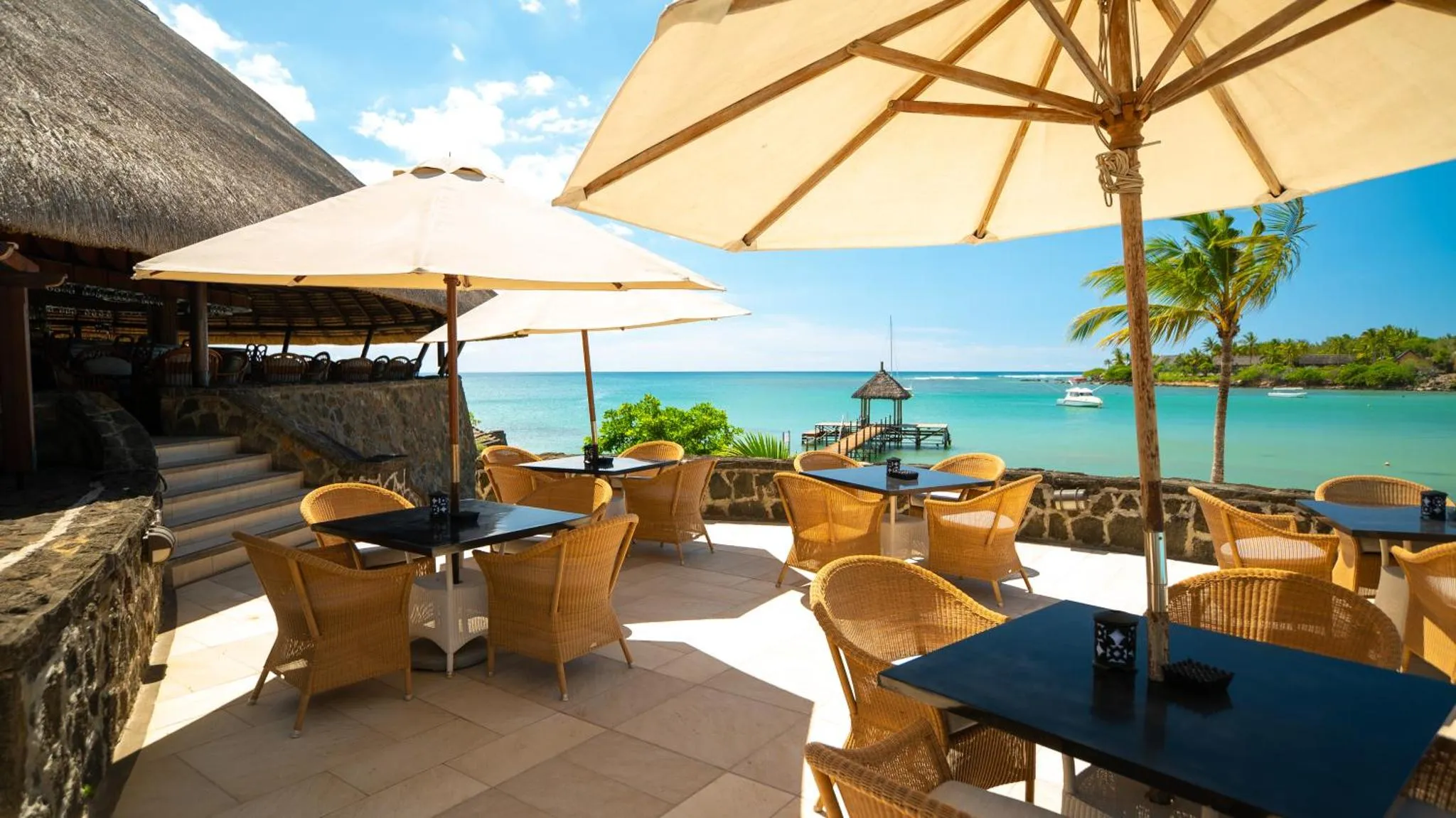 Terrasse ombragée avec tables et chaises en osier donnant sur la mer.