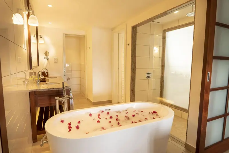 Une baignoire remplie d'eau et de pétales de fleurs se trouve dans une salle de bain lumineuse.