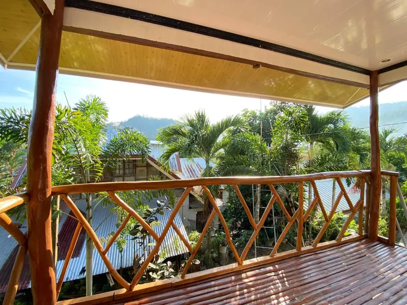 Terrasse en bois avec rambarde ajourée donnant sur une végétation luxuriante et des collines.