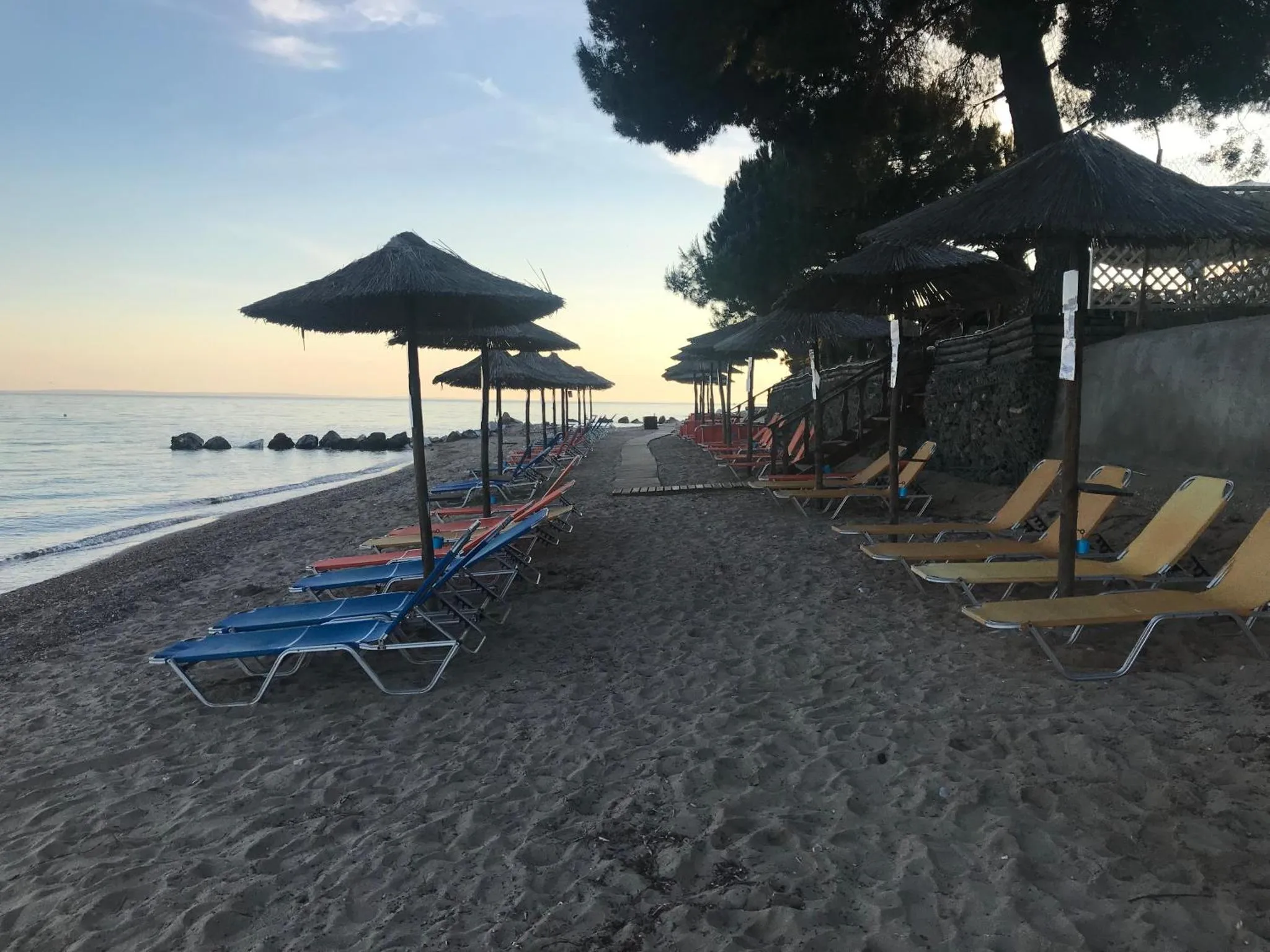 Transats alignés sur une plage de sable sombre au coucher du soleil.
