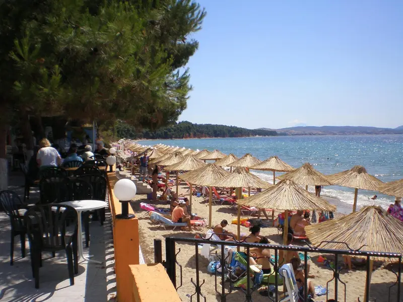 Plage ensoleillée avec parasols de paille et transats.