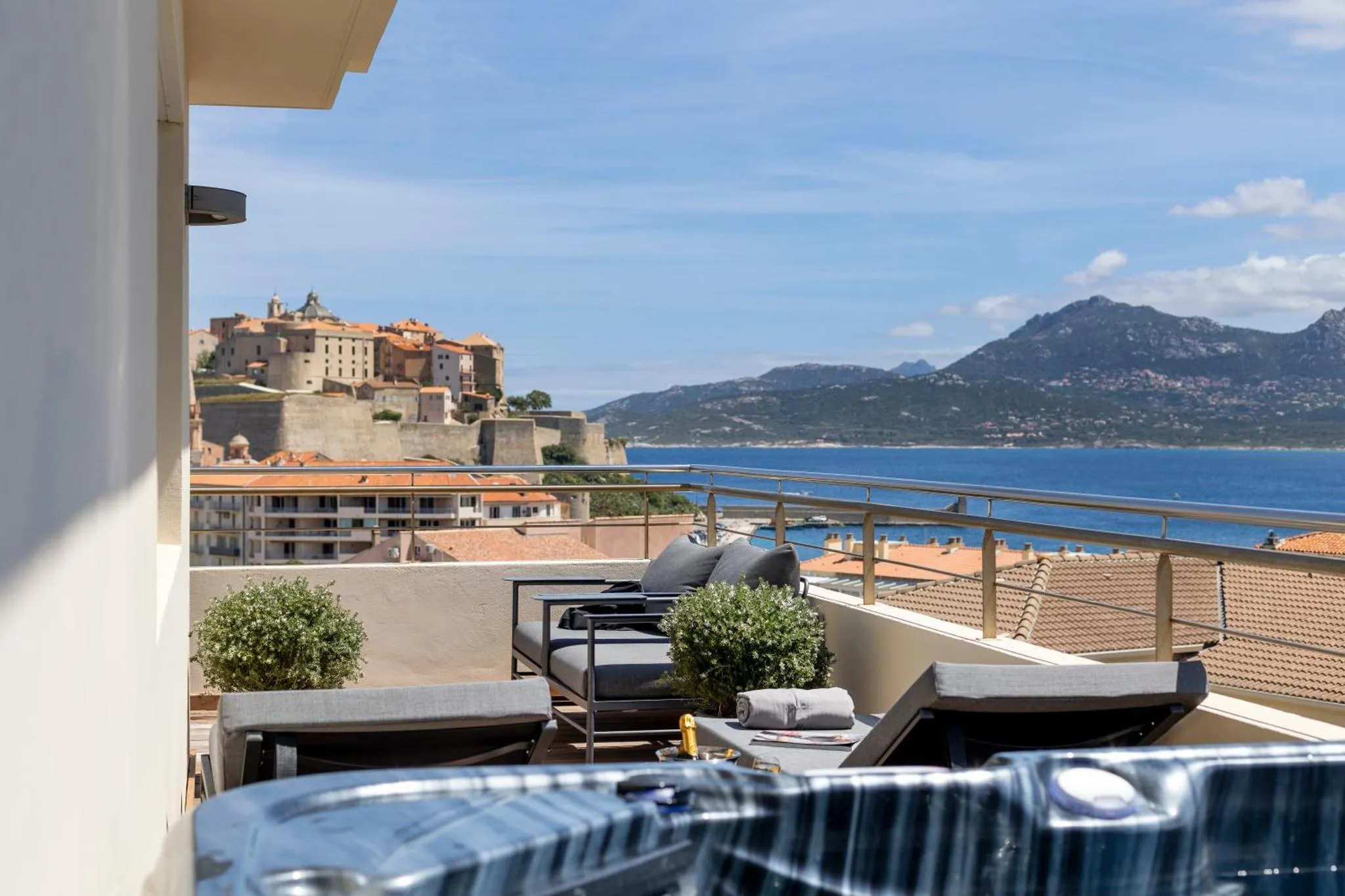 Terrasse aménagée avec transats et vue sur la mer et les montagnes.