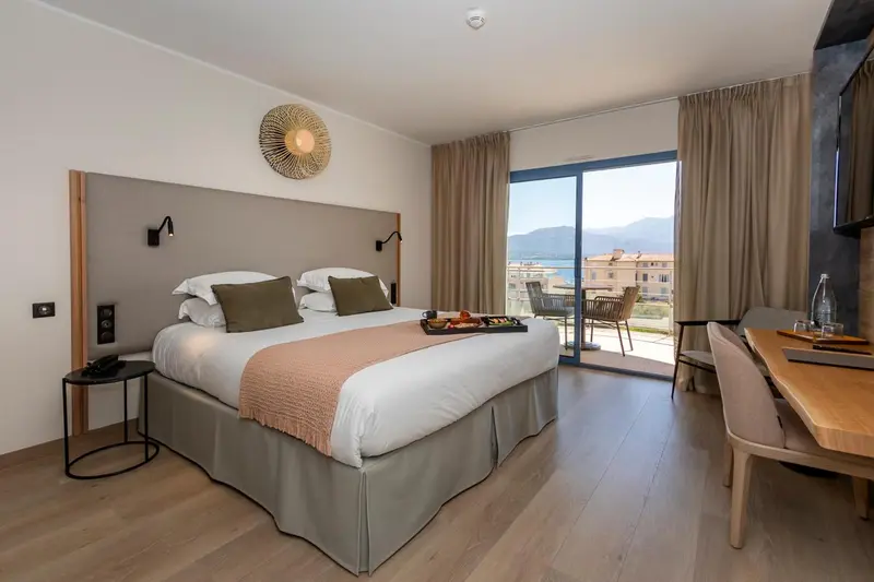 Une chambre lumineuse avec un grand lit et un balcon offrant une vue sur la mer.